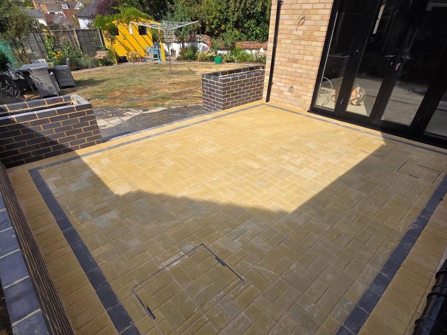 Buff block paved patio with brick walls looking out over the garden