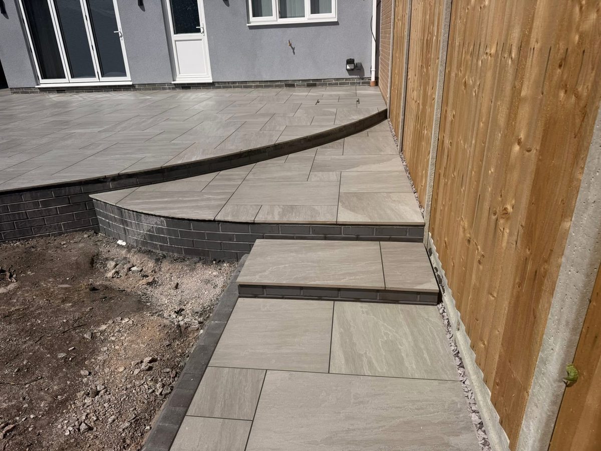 Raised porcelain patio with curved steps and a brick retaining wall